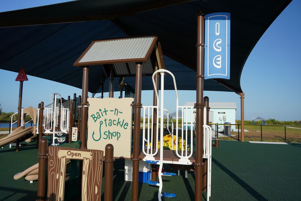 Shaded playground at Tropicana Park with a fishing-themed play structure. Signs on it read 